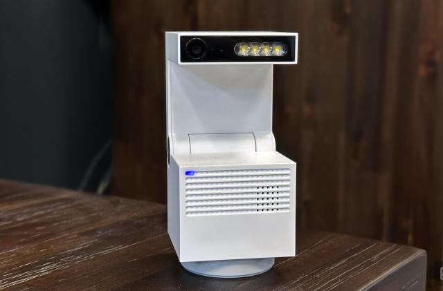 Image of the Psync Genie S AI-enabled home security camera in its default upright position on a wooden table with a wooden cabinet in the background