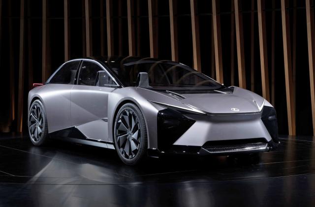 This futuristic grey, sporty Lexus EV concept has Robocop vibes and is seen on a black floor with slatted wood pillars behind it.