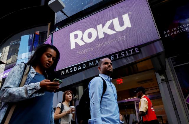 People pass by a video sign display with the logo for Roku Inc, a Fox-backed video streaming firm, that held it's IPO at the Nasdaq Marketsite in New York, U.S., September 28, 2017. REUTERS/Brendan McDermid