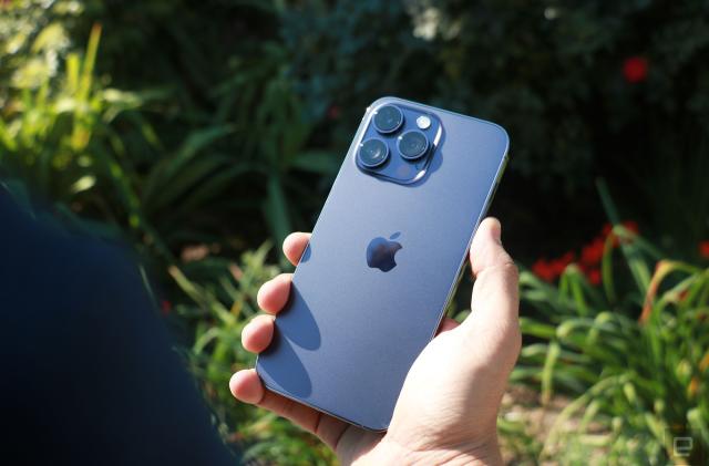 The iPhone 14 Pro Max held in front of some plants with its rear cameras facing up.