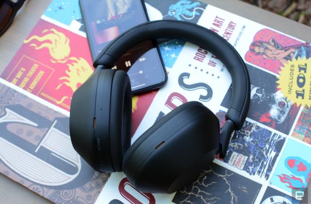 A pair of black headphones, the Sony WH-1000XM5, rest on top of a book and a smartphone.