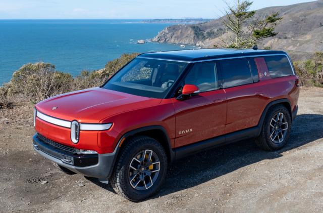 Photo of the Rivian R1S electric SUV (red) sitting by a beach with rocky shores.
