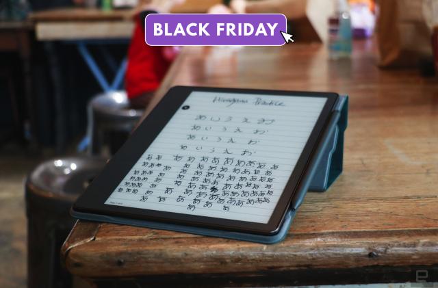 Amazon's Kindle scribe is propped up on a scarred wooden table. Handwritten characters appear on the screen. 