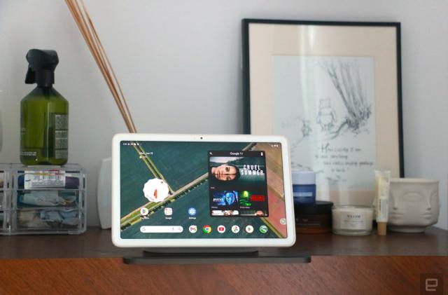 The Pixel Tablet on its dock on a walnut chest of drawers showing the Android home screen. 