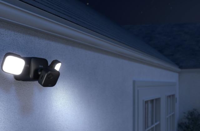 Image of the Blink Outdoor 4 with its external floodlight mount, sold separately, projecting light into the darkness. 